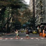 Pessoas atravessam uma rua molhada em Copacabana, no Rio de Janeiro, sob chuva, cercadas por edifícios urbanos.