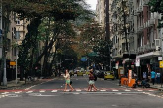 Pessoas atravessam uma rua molhada em Copacabana, no Rio de Janeiro, sob chuva, cercadas por edifícios urbanos.