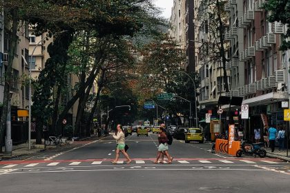 Pessoas atravessam uma rua molhada em Copacabana, no Rio de Janeiro, sob chuva, cercadas por edifícios urbanos.