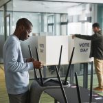 Duas pessoas preparam cabines de votação em um ambiente interno para o dia da eleição.