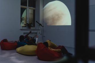 Crianças participam de uma atividade de astronomia com telescópio e projeção de um planeta em ambiente interno.