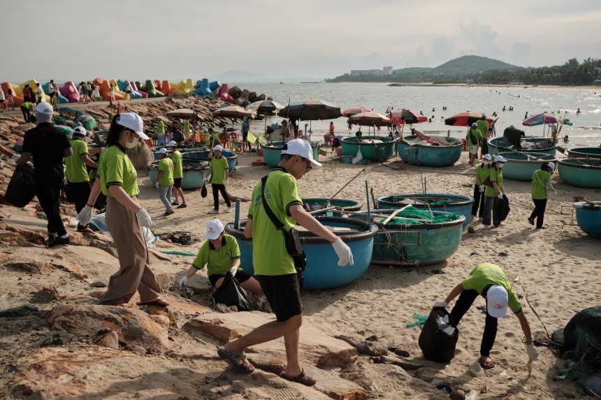 Grupo de voluntários recolhe resíduos na faixa de areia de uma praia durante uma ação de limpeza ambiental.