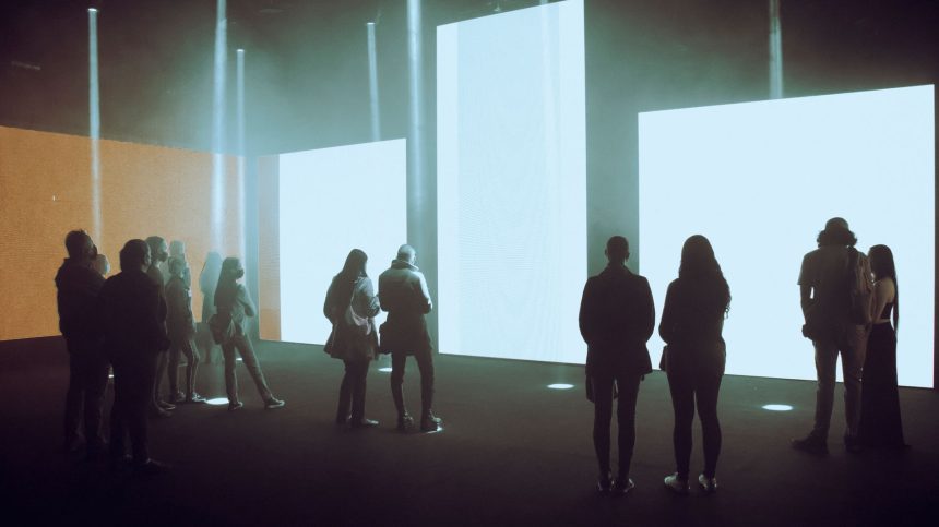 Visitantes exploram uma instalação de arte digital imersiva com grandes telas iluminadas.