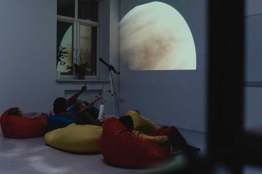 Crianças participam de uma atividade de astronomia com telescópio e projeção de um planeta em ambiente interno.