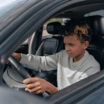 Jovem pratica direção ao volante de um carro durante uma aula de condução.