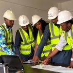 Equipe de engenheiros usando capacetes e coletes de segurança analisa plantas de um projeto de construção em ambiente interno