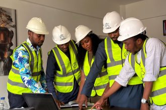 Equipe de engenheiros usando capacetes e coletes de segurança analisa plantas de um projeto de construção em ambiente interno