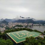 Vista aérea do Rio de Janeiro, com áreas verdes, prédios e um heliponto em primeiro plano
