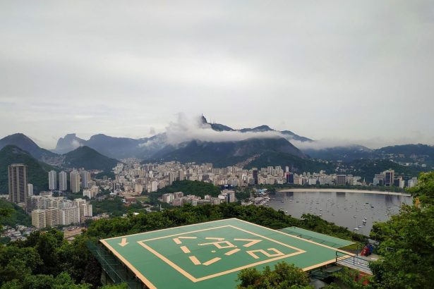 Vista aérea do Rio de Janeiro, com áreas verdes, prédios e um heliponto em primeiro plano