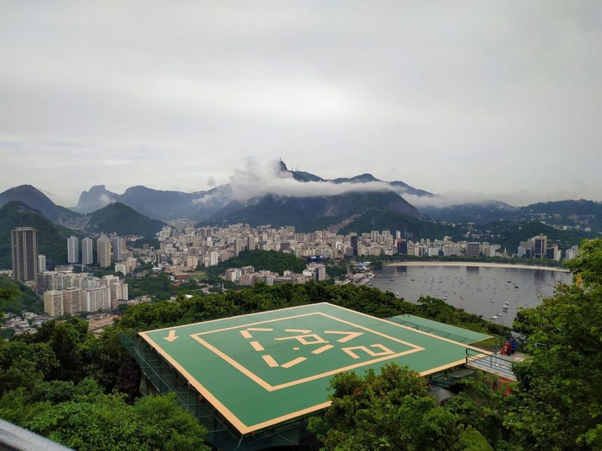 Vista aérea do Rio de Janeiro, com áreas verdes, prédios e um heliponto em primeiro plano