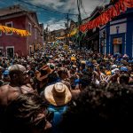 Multidão participa de uma festa de carnaval de rua no Rio de Janeiro, cercada por decorações coloridas.