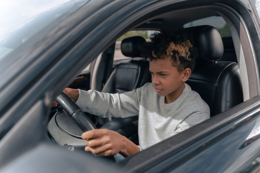 Jovem pratica direção ao volante de um carro durante uma aula de condução.
