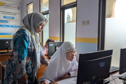 Professora orienta estudante durante atividade em um computador em um laboratório de informática.