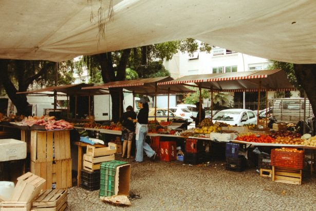 Pessoas circulam por uma feira ao ar livre no Rio de Janeiro, com barracas de produtos frescos sob uma cobertura.